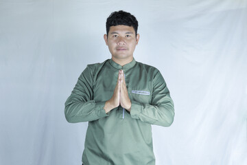 portrait of a handsome businessman. Studio shot of a man with a calm expression, hands in prayer position, wearing a muted olive-green traditional shirt against a plain white background.