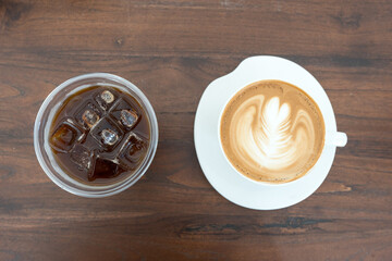 A steaming cup of latte with latte art and ice americano on a wooden table in a cozy cafe setting