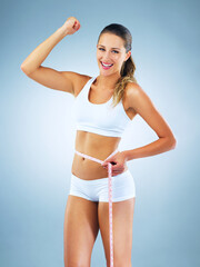 Obraz premium Happy woman, portrait and flex with measuring tape for lose weight, diet or strength in studio on a blue background. Young female person or model with smile for slim body, gym goals or achievement