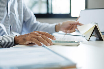 asian businessman using smart phone working on desk review documents report, ckecking appointment in note book and meeting online via laptop in office