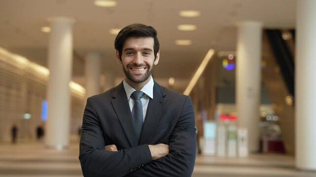 Business man walking at center while standing with arm folded at modern mall. Smiling happy investor looking at camera with confident while crossing arms at hall with blurring background. Exultant.