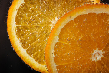 Slice of orange fruit in water with gas bubbles. Refreshing citrus drink, cocktail. Macro.