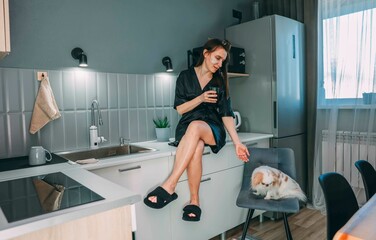 Fototapeta premium relaxed woman enjoying a glass of water in a modern kitchen, with a small dog, concept of daily hydration