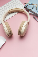 Wireless headphones, keyboard, computer mouse, eyeglasses, pen and notebooks on pink background
