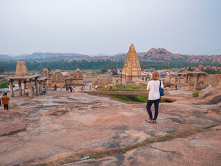 Woman exploring amazing temple complex at Hampi, world famous unesco site. Tourist walking among ruins stone walls gateways in Karnataka, India