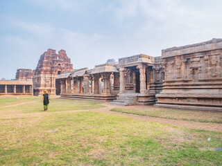 Woman exploring amazing temple complex at Hampi, world famous unesco site. Tourist walking among ruins stone walls gateways in Karnataka, India