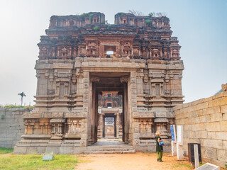 Woman exploring amazing temple complex at Hampi, world famous unesco site. Tourist walking among ruins stone walls gateways in Karnataka, India