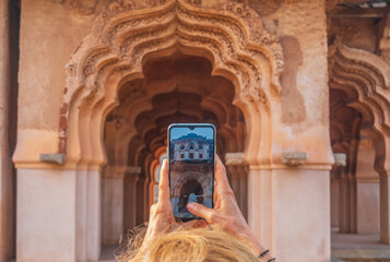 Woman taking photo of amazing temples at Hampi, world famous unesco site. Tourist using mobile phone among ruins stone walls gateways in Karnataka, India
