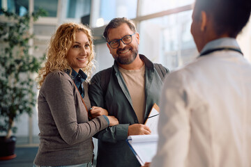 Happy woman and her husband talking to general practitioner at doctor's office.