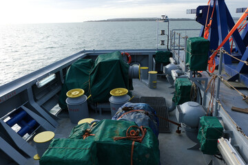 View on mooring winches in aft stern manoeuvring station with bollards, bitts and ropes of heavy load carrier vessel. Winches and windlass are covered with green tarpaulin.