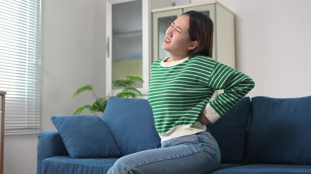 Young woman suffering from back pain while sitting on sofa