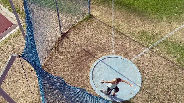 High angle: Young woman athlete throws discus on grass sports field