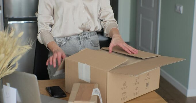 Young woman buyer opening parcel box at home. Female customer shopper receiving online shop purchase buying clothes unpacking delivery package.