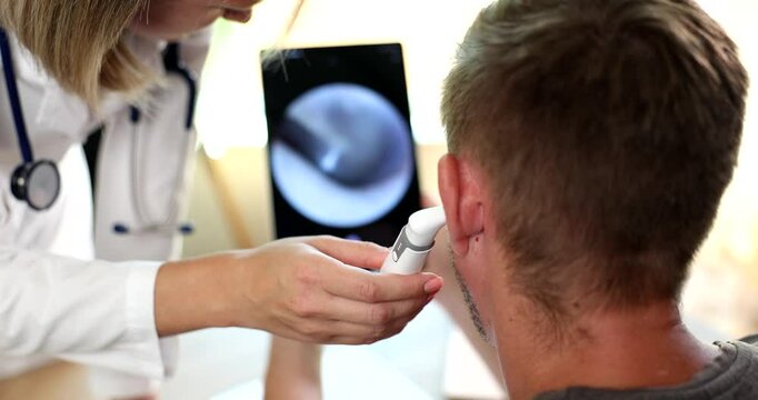Female doctor uses digital otoscope to check patient ear in clinic. Man undergoes hearing organs medical checkup with specialist in hospital