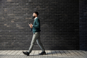 Side view of smart casual businessman in rush walking with smart phone in hands.