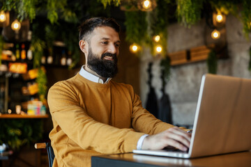 Portrait of happy entrepreneur in smart causal sitting in coffee shop and typing on laptop.