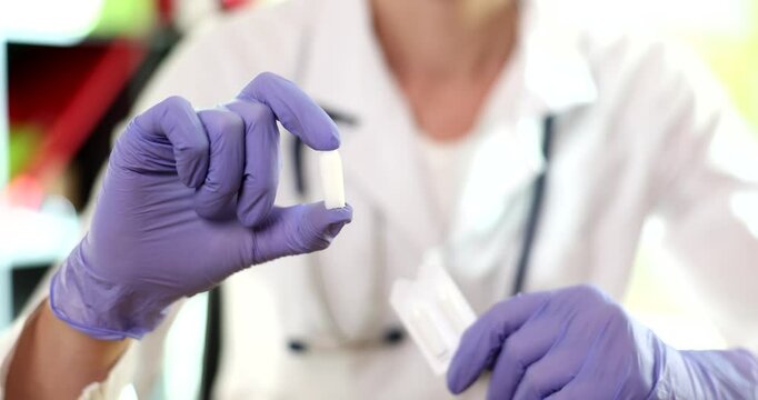 Woman physician holds box of suppositories in hands at appointment. Experienced doctor describes benefits of prescribed suppositories. Slow motion