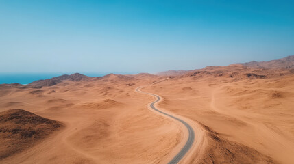Fototapeta premium Winding desert road stretches through vast sandy landscape under clear blue sky