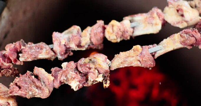 Small pieces of marinated mutton meat on skewers rest over open grill flame. Fat from meat drips onto hot coals creating small bursts of smoke