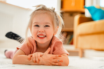 Fototapeta premium Cute little child girl 3 years old is sitting at home on the carpet in the children's room