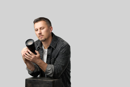 Photographer Inspecting Camera Lens. A man in a denim shirt carefully examines a camera
