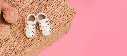 Sandals shoes for a child on a wicker basket on a pink background, the concept of childhood and...