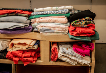 Colorful folded fabric pieces stacked on wooden shelves in indoor store