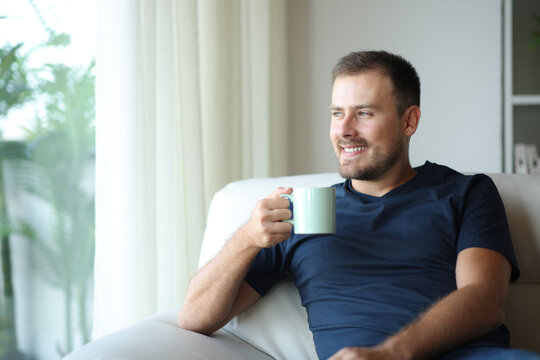 Happy man at home drinking coffee or tea looking through a window