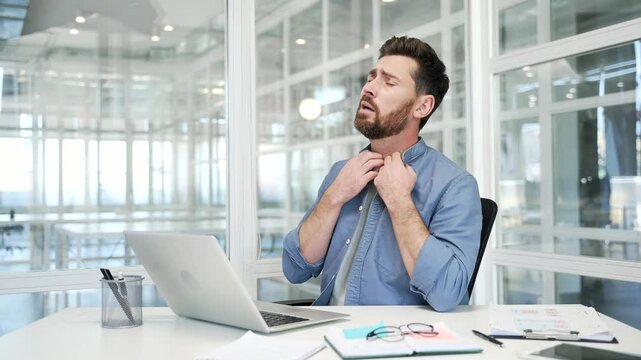 Businessman is hot while sitting at desk at the workplace in a modern business office. The man waves his hands like a fan, cannot concentrate on work, because the air conditioner in the room is broken