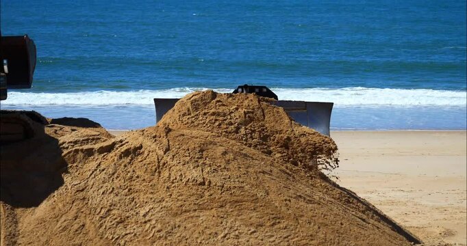 Bulldozer and crane handling sand to combat beach erosion.