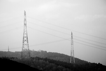 High voltage line. The city's energy transmission line. Electric towers in foggy sky. Black and...