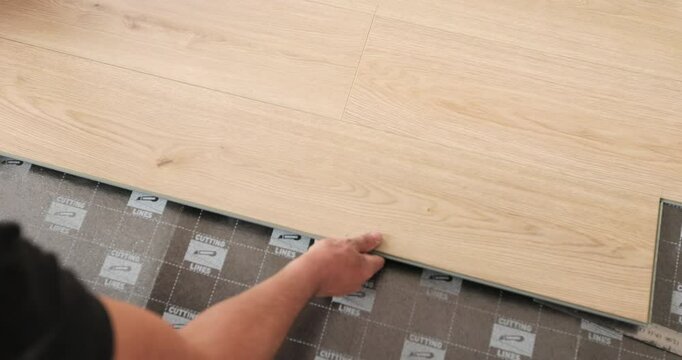 Laying laminate flooring in a new apartment, master man installing flooring on black sheets.