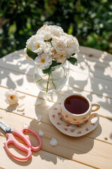 Summer still life. Beautiful roses flowers stand in a vase on a wooden table with a cup of tea.
Relaxation in the village on a sunny day. The joy of summer.