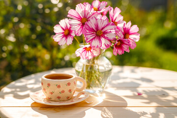 Summer still life. Beautiful cosmos flowers stand in a vase on a wooden table with a cup of tea.
Relaxation in the village on a sunny day. The joy of summer.