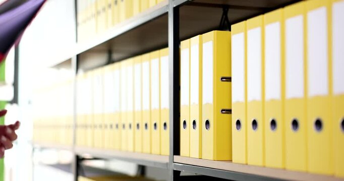 Woman hand takes red ring binder from shelf in corporate archive. Female office employee picks color folder with documents in company storage