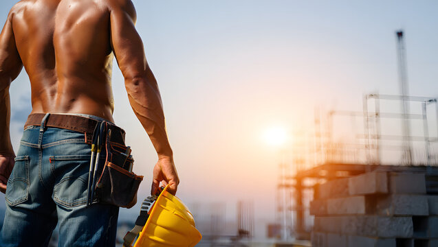 Muskul&ouml;ser Bauarbeiter mit Helm bei Sonnenuntergang auf Baustelle
