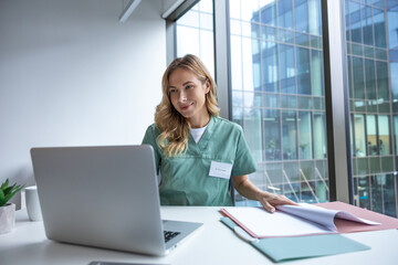 Female doctor sitting at table with laptop in workplace in hospital
