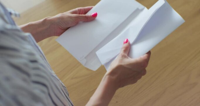 Close up female hands putting letter in envelop return form. Woman sends a return form by letter.