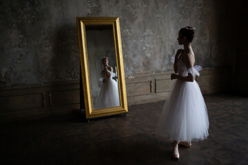 Beautiful ballerina in a white dress looks in the mirror.