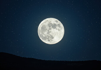 Fototapeta premium A stunning view of a full moon, illuminated against a dark, starry night sky.