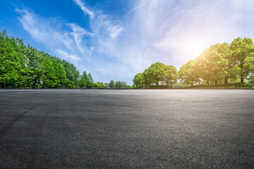 Empty asphalt road ground and lush green trees under a sunny blue sky