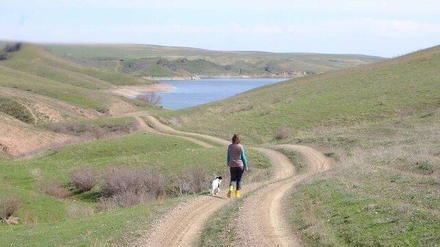 A female tourist and her dog friend walk along the road leading to the blue lake in spring. Kurtinskoye Reservoir Kazakhstan Almaty