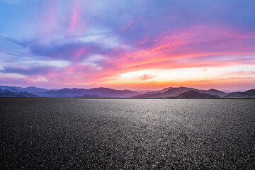 Empty asphalt road ground and mountain range with dramatic sunset sky clouds