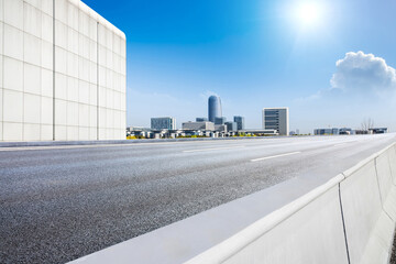 Empty asphalt road and city skyline with modern buildings scenery under a sunny blue sky