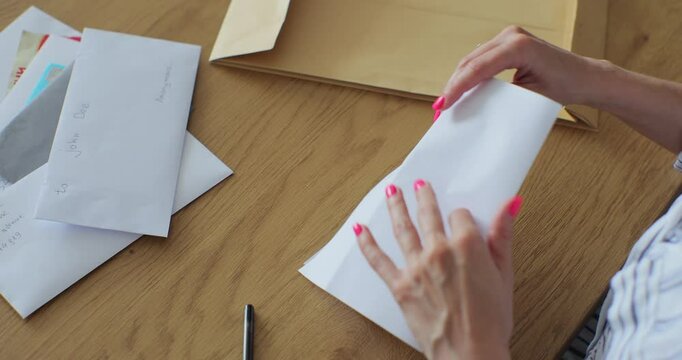 Close up female hands putting letter in envelop return form. Woman sends a return form by letter.