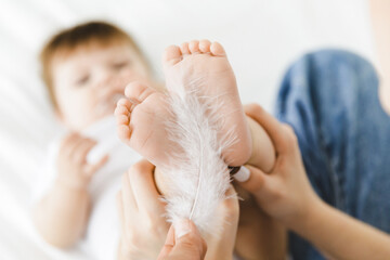 A joyful moment when a mother playfully tickles her baby's feet with a feather. Perfect for showing...