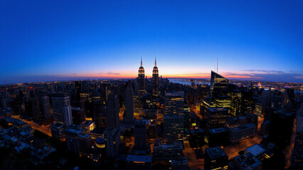 Naklejka premium Night cityscape: illuminated buildings under dark blue sky. Urban metropolis with vast skyline and bright city lights creating a vibrant night scene.