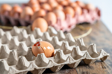Broken egg leaking in carton with whole eggs in background