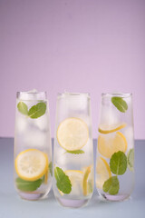 refreshing glasses of lemon and mint-infused water against a soft pastel purple background, highlighting their vibrant colors and fresh ingredients in a calm, inviting composition. tranquil, ambient