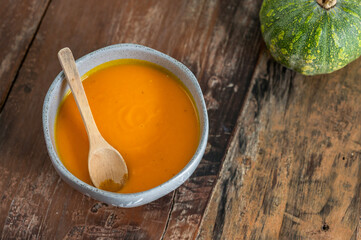 Pumpkin soup in bowl with pumpkin on rustic wooden table